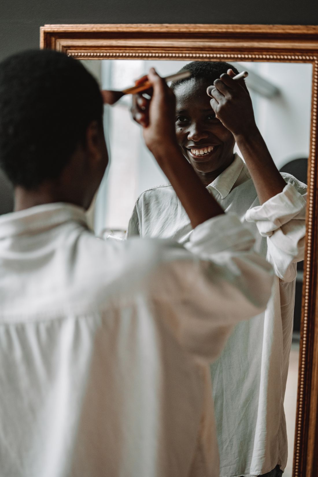 Une femme souriante se maquille devant un miroir